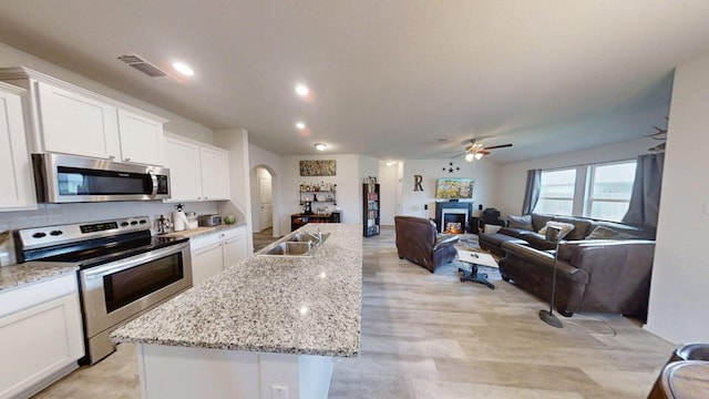 183 Beth Ann Loop, Taylor, TX 76574 - kitchen featuring stainless steel appliances, arched walkways, a kitchen island with sink, white cabinets, and a warm lit fireplace