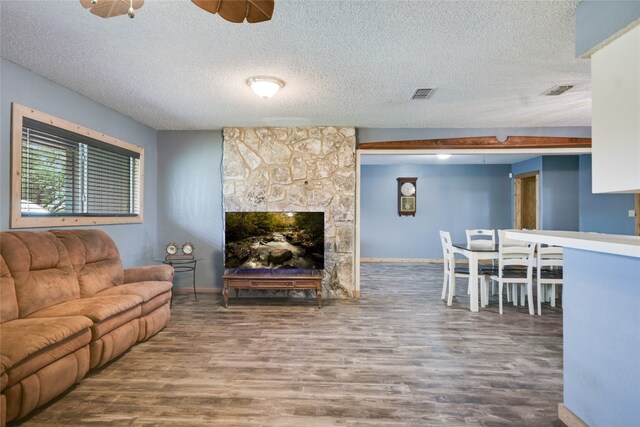838 Pine Ln, Cottonwood Shores, TX 78657 - living room with wood finished floors, a textured ceiling, baseboards, ceiling fan, and a stone fireplace