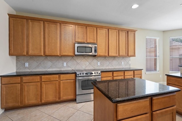 13617 Sun Dapple Ct, Manor, TX 78653 - kitchen with appliances with stainless steel finishes, backsplash, brown cabinetry, dark stone countertops, and a kitchen island