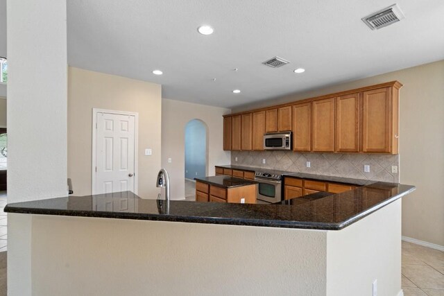 13617 Sun Dapple Ct, Manor, TX 78653 - kitchen featuring stainless steel appliances, arched walkways, a spacious island, decorative backsplash, and brown cabinets