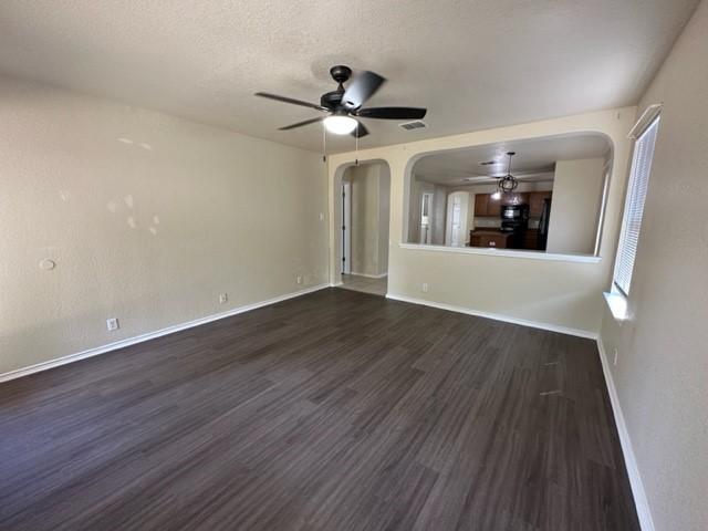 221 Roadrunner Ave, New Braunfels, TX 78130 - unfurnished living room featuring ceiling fan, arched walkways, dark wood-style floors, baseboards, and a textured ceiling