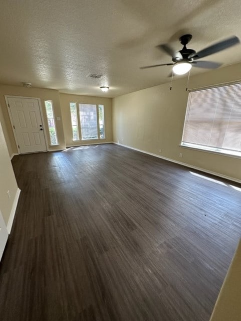 221 Roadrunner Ave, New Braunfels, TX 78130 - unfurnished living room with a textured ceiling, dark wood-type flooring, ceiling fan, and baseboards