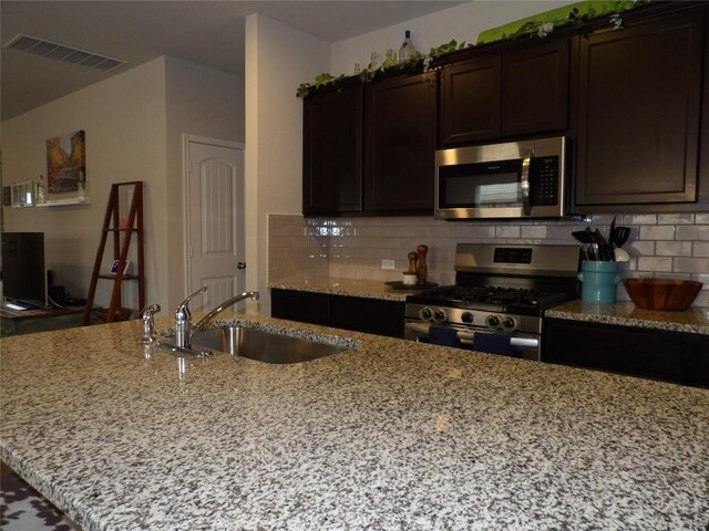 3097 Blantyre Bnd, Round Rock, TX 78664 - kitchen featuring stainless steel appliances, a sink, light stone countertops, decorative backsplash, and dark brown cabinetry