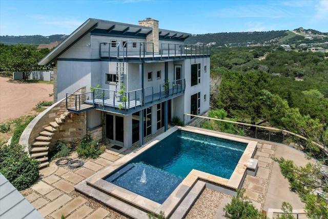 8207 Moon Rise Trl, Jonestown, TX 78645 - rear view of property featuring a balcony, stairway, stucco siding, an outdoor pool, and a chimney