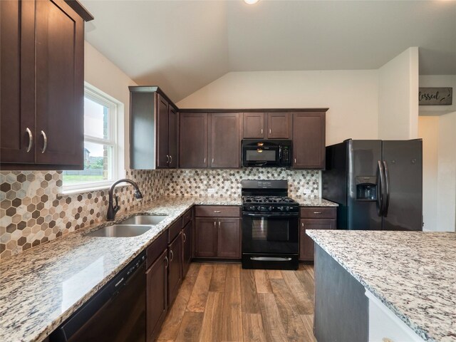 7632 Lombardy Loop, Round Rock, TX 78665 - kitchen with black appliances, a sink, wood finished floors, light stone counters, and vaulted ceiling
