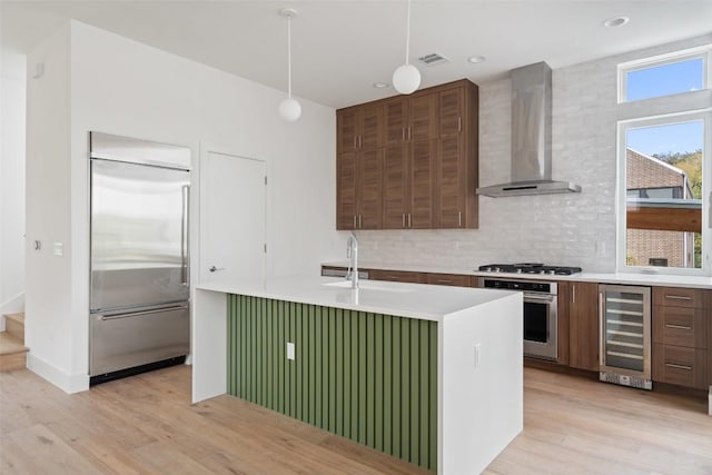 900 S 2nd St Unit 21, Austin, TX 78704 - kitchen with appliances with stainless steel finishes, beverage cooler, wall chimney range hood, a sink, and light wood-style flooring
