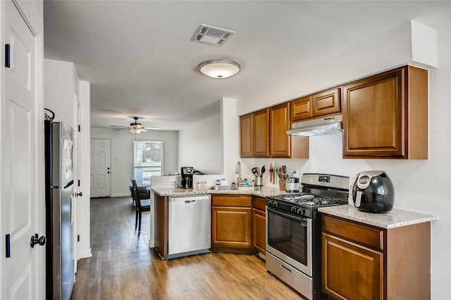 312 W William Cannon Dr, Austin, TX 78745 - kitchen with stainless steel appliances, under cabinet range hood, a peninsula, a sink, and brown cabinetry