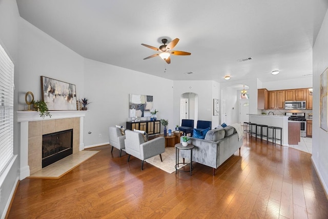 805 Meadow Bluff Ct, Round Rock, TX 78665 - living area featuring arched walkways, light wood finished floors, a ceiling fan, and a tiled fireplace