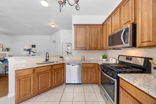 805 Meadow Bluff Ct, Round Rock, TX 78665 - kitchen featuring stainless steel appliances, a sink, a peninsula, brown cabinetry, and light tile patterned floors
