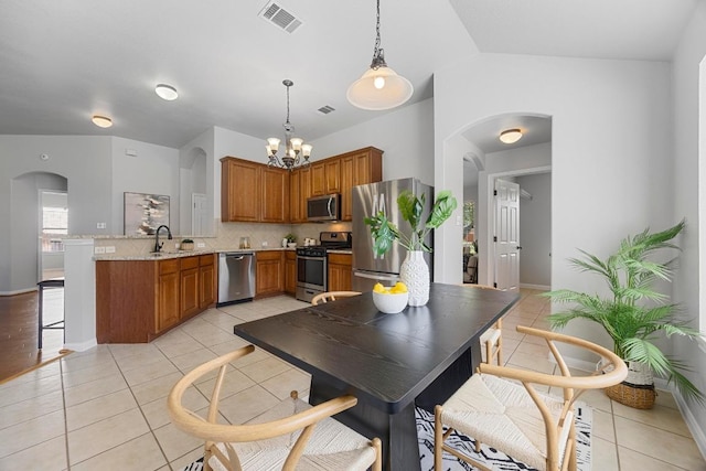 805 Meadow Bluff Ct, Round Rock, TX 78665 - kitchen with stainless steel appliances, a peninsula, light tile patterned flooring, arched walkways, and brown cabinetry