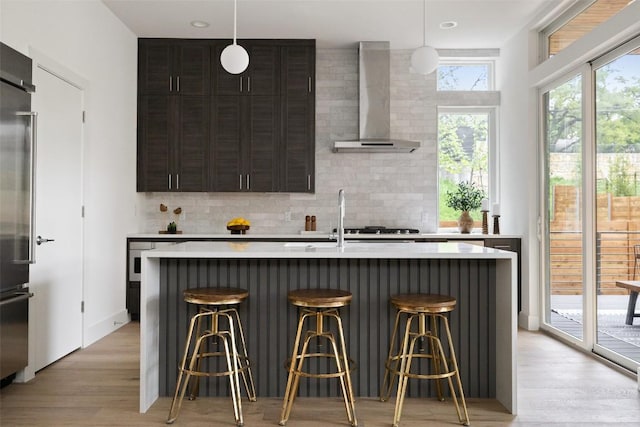 900 S 2nd St Unit 20, Austin, TX 78704 - kitchen featuring wall chimney range hood, light countertops, backsplash, light wood-style flooring, and a kitchen breakfast bar