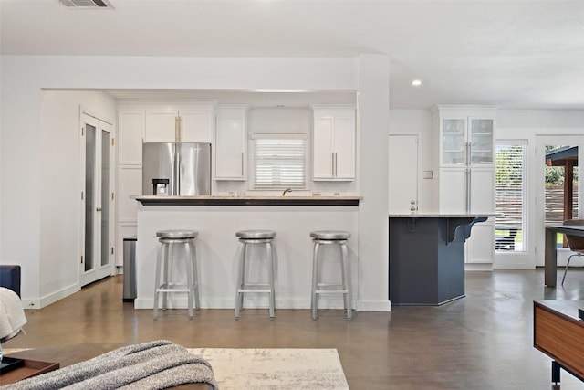7517 Saint Louis St, Austin, TX 78757 - kitchen with stainless steel fridge with ice dispenser, white cabinetry, a breakfast bar, concrete flooring, and recessed lighting