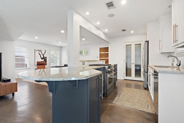 7517 Saint Louis St, Austin, TX 78757 - kitchen featuring stainless steel appliances, a sink, a kitchen breakfast bar, white cabinets, and light stone countertops