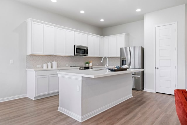 9904 Comely Bnd, Manor, TX 78653 - kitchen with appliances with stainless steel finishes, light wood-style flooring, decorative backsplash, light countertops, and an island with sink