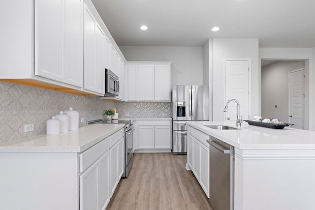 9904 Comely Bnd, Manor, TX 78653 - kitchen featuring appliances with stainless steel finishes, a kitchen island with sink, light countertops, white cabinets, and light wood-style floors