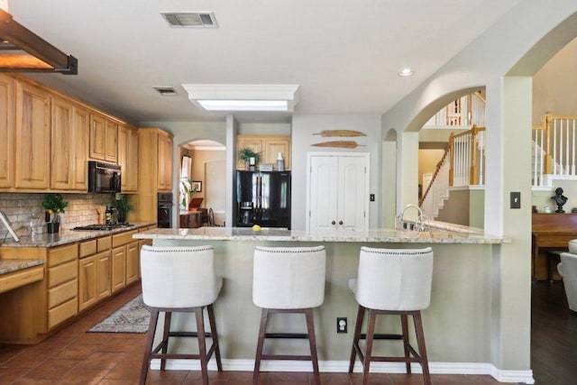 20737 Kearney Hill Rd, Pflugerville, TX 78660 - kitchen featuring black appliances, arched walkways, a breakfast bar area, backsplash, and light stone counters