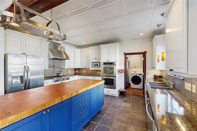 6002 Rain Creek Pkwy, Austin, TX 78759 - kitchen with washer / dryer, stainless steel appliances, blue cabinets, wall chimney exhaust hood, and butcher block countertops
