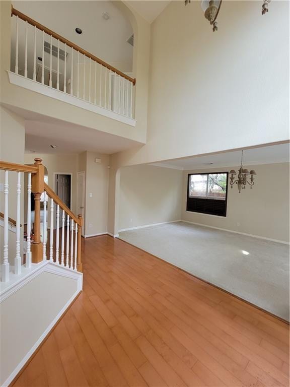 unfurnished living room featuring a high ceiling, a chandelier, baseboards, wood finished floors, and stairway