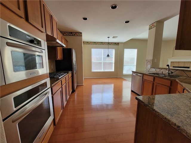 kitchen featuring a sink, stainless steel appliances, under cabinet range hood, brown cabinets, and light wood-style flooring