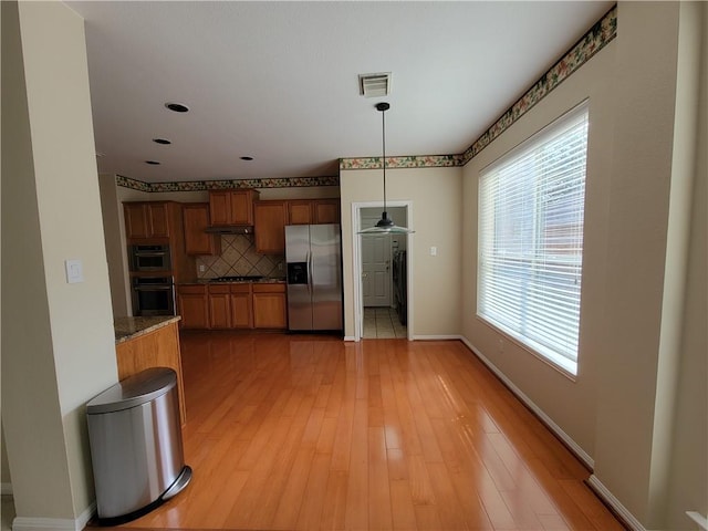 kitchen featuring stainless steel appliances, brown cabinetry, decorative backsplash, baseboards, and pendant lighting