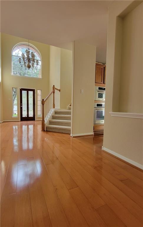 entryway with light wood-style floors, stairway, a chandelier, baseboards, and french doors