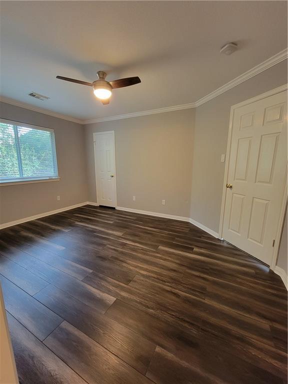 spare room featuring dark wood finished floors, baseboards, crown molding, and a ceiling fan