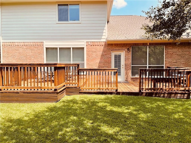 rear view of property featuring brick siding, a deck, a yard, and a shingled roof