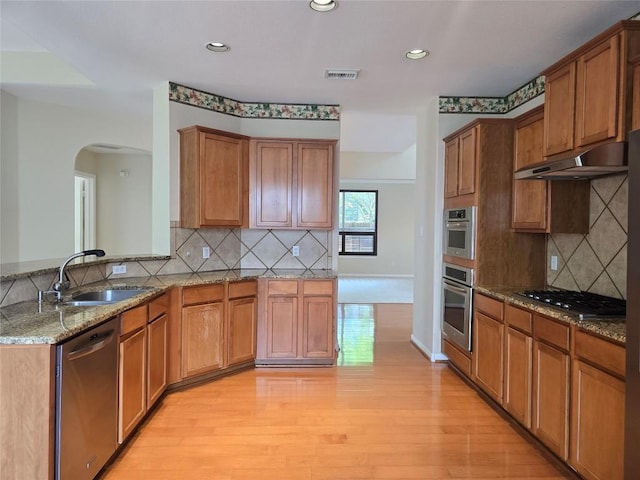 1411 Hunter Ace Way, Cedar Park, TX 78613 - kitchen with appliances with stainless steel finishes, under cabinet range hood, arched walkways, light wood-style floors, and light stone counters