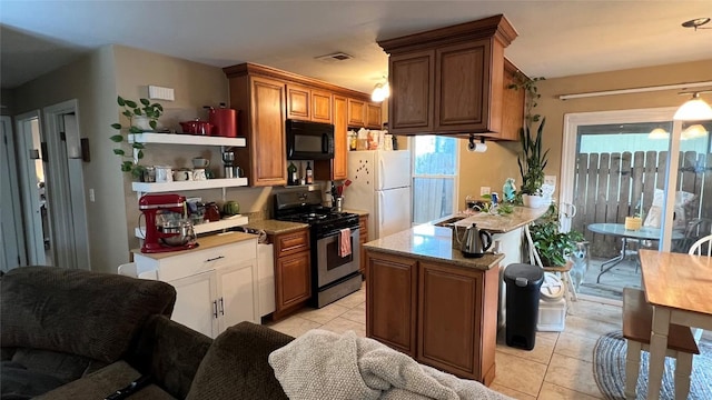 3307 Whitepine Dr, Austin, TX 78757 - kitchen with stainless steel range with gas cooktop, black microwave, freestanding refrigerator, light tile patterned flooring, and a peninsula