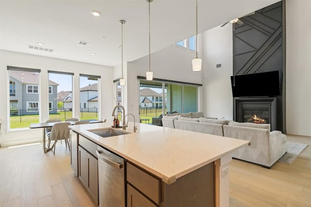 2905 Canto Trce, Leander, TX 78641 - kitchen with stainless steel dishwasher, light wood-type flooring, decorative light fixtures, a kitchen island with sink, and light stone countertops