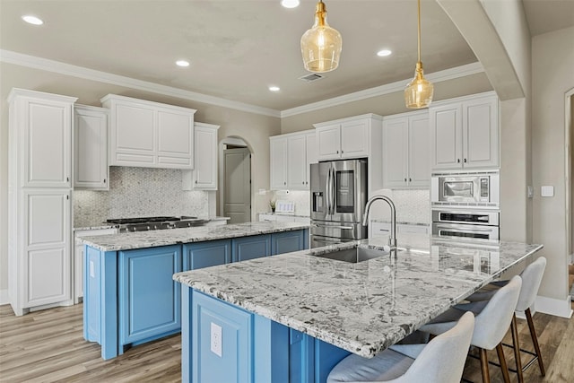 101 Aldea St, Georgetown, TX 78633 - kitchen featuring a spacious island, appliances with stainless steel finishes, arched walkways, blue cabinets, and light wood-type flooring
