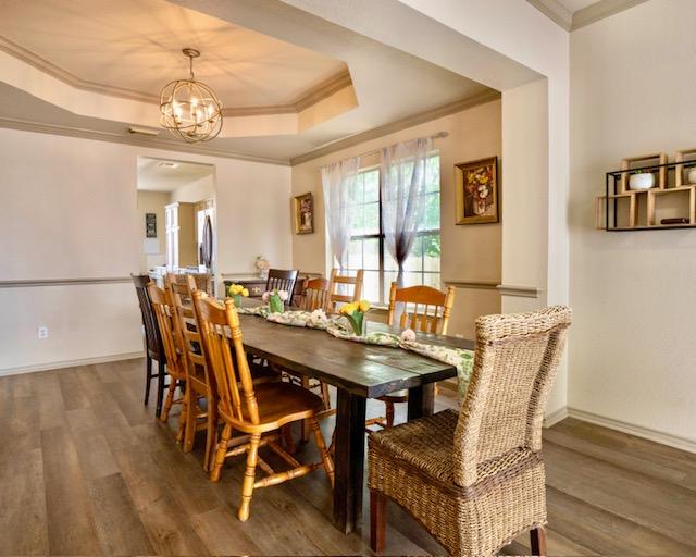 1406 Apache Cv, Pflugerville, TX 78660 - dining area featuring wood finished floors, a raised ceiling, a chandelier, and crown molding