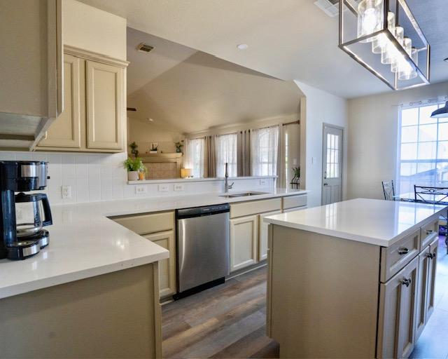 1406 Apache Cv, Pflugerville, TX 78660 - kitchen featuring dishwasher, wood finished floors, light countertops, decorative light fixtures, and vaulted ceiling