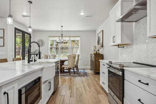 2 Basswood Cir, Wimberley, TX 78676 - kitchen featuring appliances with stainless steel finishes, wall chimney range hood, tasteful backsplash, light wood finished floors, and white cabinetry