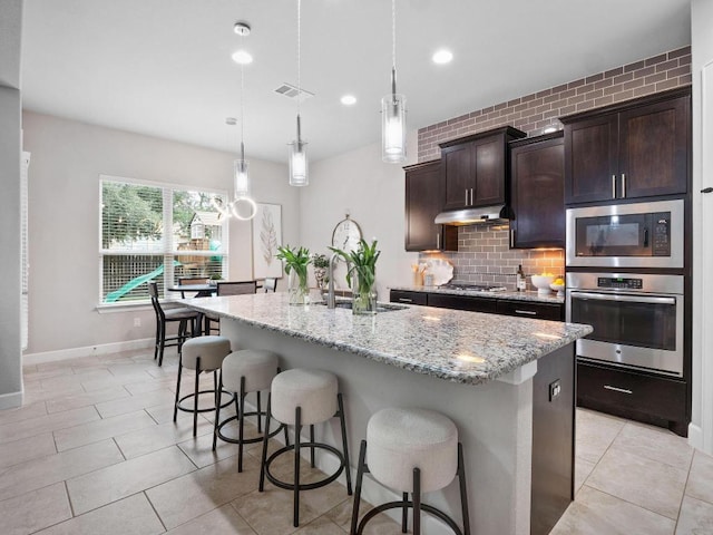 116 Claiborne Lake Ln, Georgetown, TX 78628 - kitchen with appliances with stainless steel finishes, light stone counters, a breakfast bar, under cabinet range hood, and recessed lighting