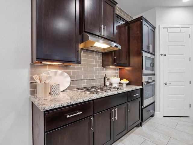 116 Claiborne Lake Ln, Georgetown, TX 78628 - kitchen with stainless steel appliances, under cabinet range hood, backsplash, dark brown cabinets, and light stone countertops