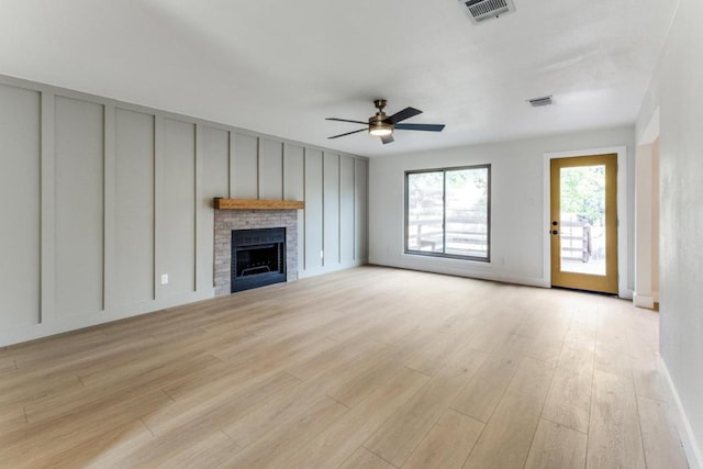 7702 Turquoise Trl, Austin, TX 78749 - unfurnished living room with a decorative wall, light wood-type flooring, a brick fireplace, a ceiling fan, and baseboards
