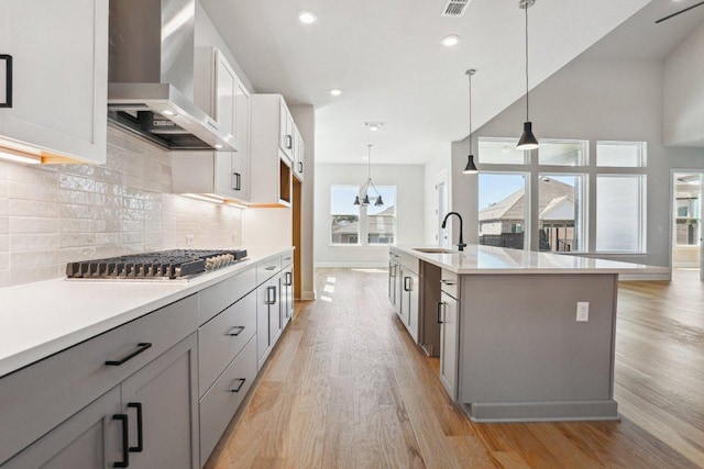 16825 Roselin Dr, Austin, TX 78738 - kitchen with wall chimney exhaust hood, a sink, stainless steel gas cooktop, light wood finished floors, and decorative backsplash