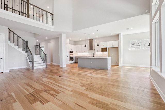 16825 Roselin Dr, Austin, TX 78738 - unfurnished living room featuring light wood-style floors, baseboards, stairway, a sink, and a high ceiling