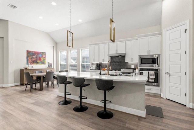 1504 Saddlespur Ln, Leander, TX 78641 - kitchen with appliances with stainless steel finishes, vaulted ceiling, decorative backsplash, light countertops, and a kitchen island with sink