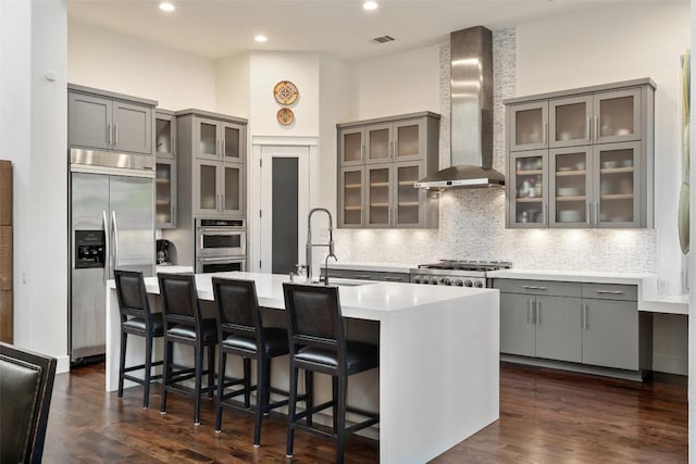104 Sendera Bonita, Lakeway, TX 78734 - kitchen featuring appliances with stainless steel finishes, wall chimney exhaust hood, gray cabinets, a kitchen island with sink, and recessed lighting