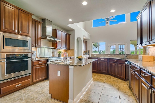 10524 Roy Butler Dr, Austin, TX 78717 - kitchen featuring stainless steel appliances, wall chimney exhaust hood, a ceiling fan, dark stone countertops, and backsplash