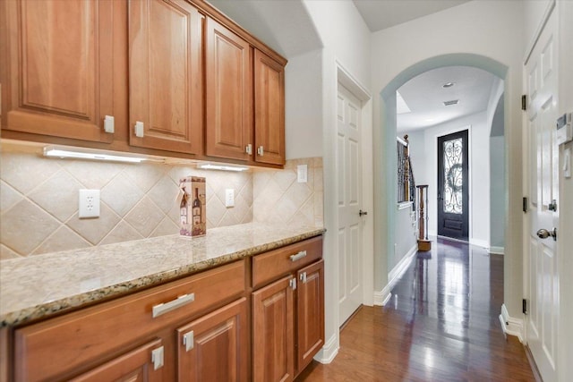10524 Roy Butler Dr, Austin, TX 78717 - kitchen with arched walkways, decorative backsplash, light stone counters, brown cabinets, and dark wood finished floors
