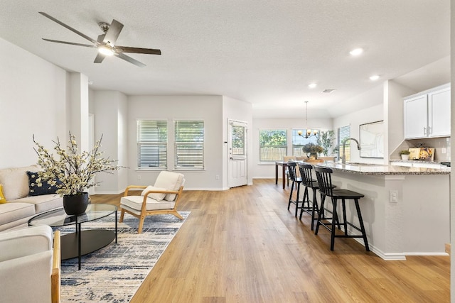 107 Nathaniel Dr, Taylor, TX 76574 - living room with light wood finished floors, a chandelier, a ceiling fan, baseboards, and a textured ceiling