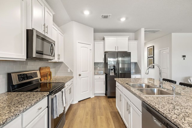 107 Nathaniel Dr, Taylor, TX 76574 - kitchen featuring stainless steel appliances, a sink, white cabinetry, light wood-type flooring, and tasteful backsplash
