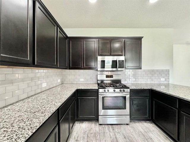 2721 Bridekirk Dr, Round Rock, TX 78664 - kitchen featuring appliances with stainless steel finishes, light stone countertops, light wood-style flooring, backsplash, and a textured ceiling
