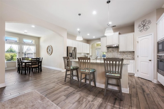213 Russet Trl, Georgetown, TX 78628 - kitchen with arched walkways, dark wood-style floors, backsplash, a kitchen breakfast bar, and white cabinetry
