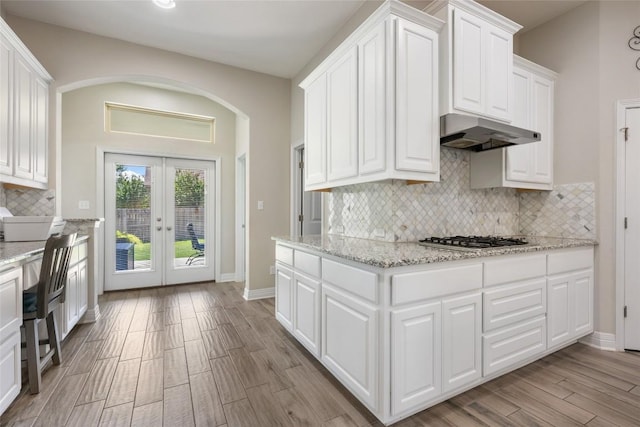 213 Russet Trl, Georgetown, TX 78628 - kitchen featuring stainless steel gas cooktop, under cabinet range hood, french doors, arched walkways, and white cabinetry