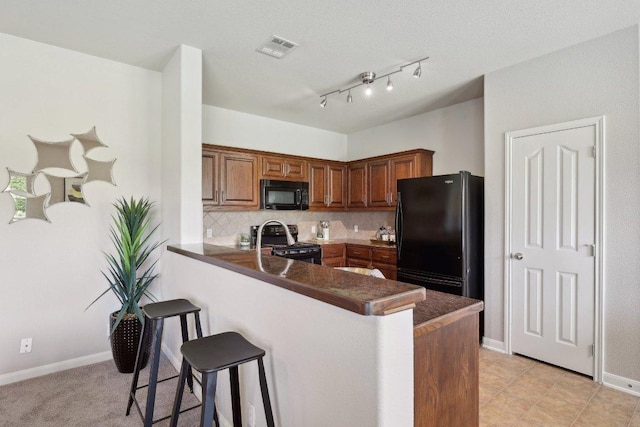 1207 Tricia Cv, Hutto, TX 78634 - kitchen with black appliances, a kitchen bar, a peninsula, dark countertops, and tasteful backsplash