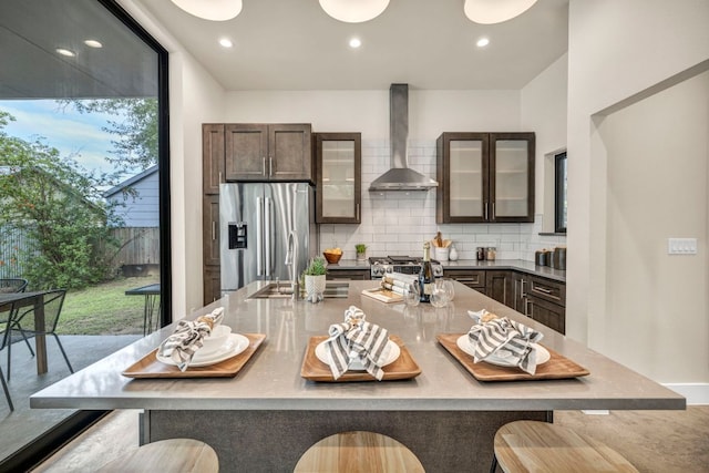803 Josephine St, Austin, TX 78704 - kitchen with wall chimney range hood, stainless steel fridge with ice dispenser, backsplash, dark brown cabinetry, and a kitchen breakfast bar